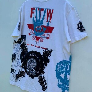 May include: White t-shirt with a graphic print of a hand with the text "FTW" and "4 year anniversary" in a red box. The shirt also has a graphic print of a skull, a guitar, and the text "We do our part".