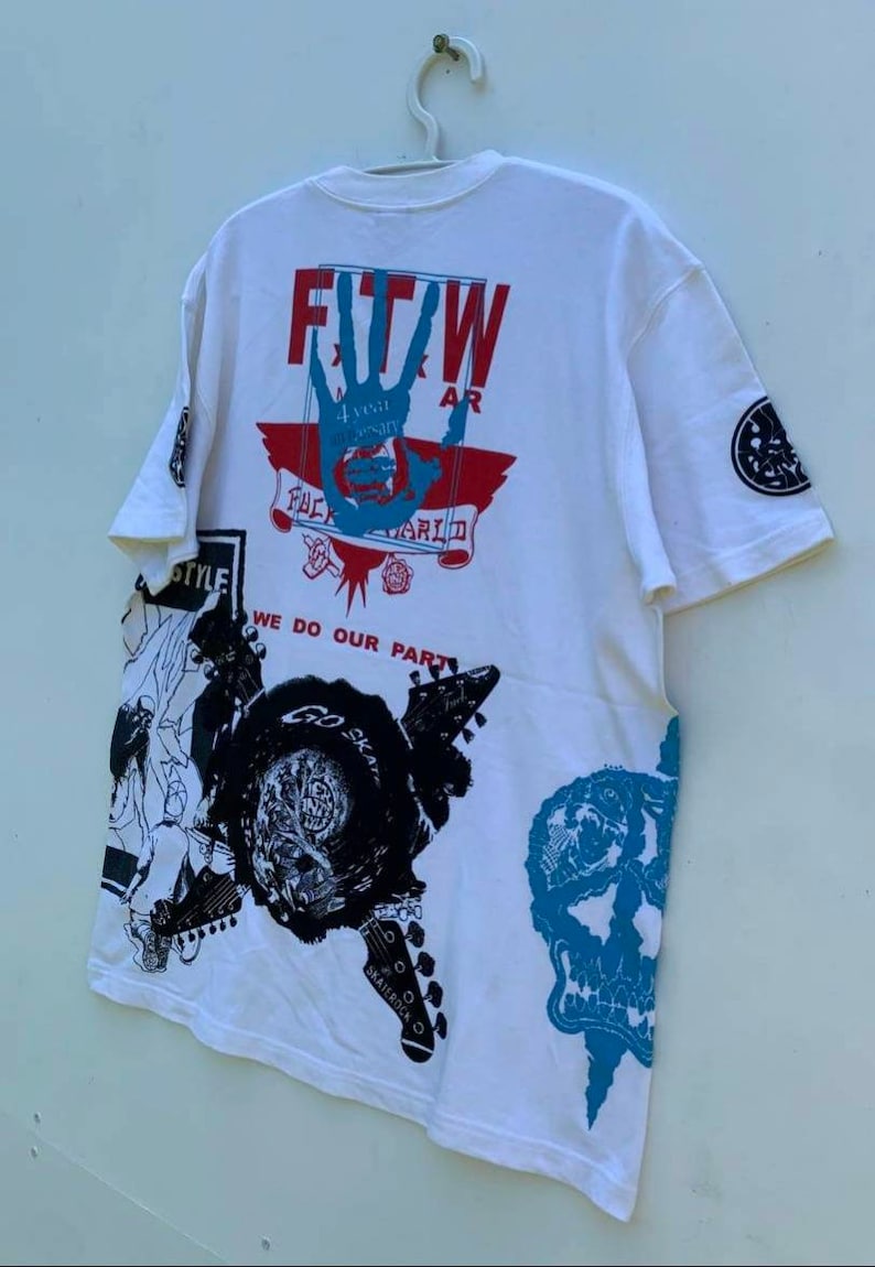 May include: White t-shirt with a graphic print of a hand with the text "FTW" and "4 year anniversary" in a red box. The shirt also has a graphic print of a skull, a guitar, and the text "We do our part".