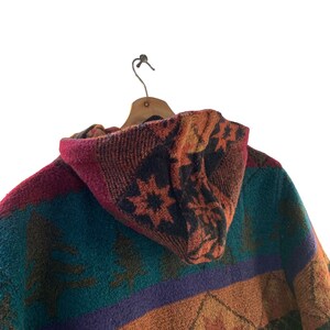 May include: A hooded jacket with a colorful geometric pattern in shades of red, orange, teal, purple, and brown. The jacket has a drawstring hood and a woven texture.