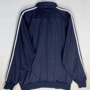 May include: A navy blue jacket with white stripes down the sleeves. The jacket has a zipper closure and a ribbed hem.