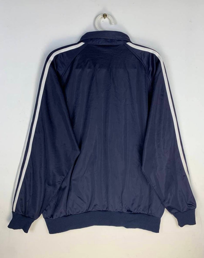 May include: A navy blue jacket with white stripes down the sleeves. The jacket has a zipper closure and a ribbed hem.