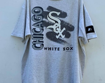 Puede incluir: Una camiseta gris con un gráfico en blanco y negro del logotipo de los Chicago White Sox. El logotipo es una "S" estilizada con un bate de béisbol y las palabras "Chicago" y "White Sox".