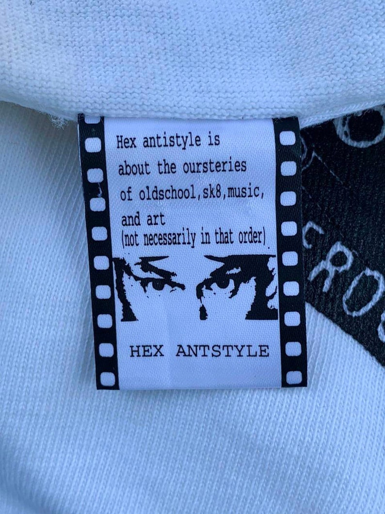 May include: White clothing tag with black text that reads "Hex antistyle is about the oursteries of oldschool, sk8, music, and art (not necessarily in that order)" and "HEX ANTSTYLE". The tag features a black and white illustration of two eyes with a single teardrop.