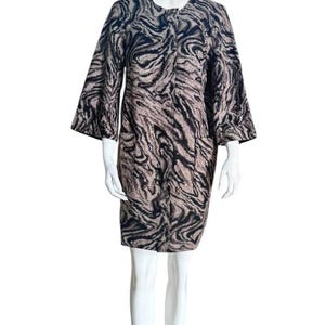May include: A knee-length dress with a black and tan swirled pattern. The dress has a round neckline, three-quarter sleeves, and two front pockets. The dress is displayed on a white mannequin.
