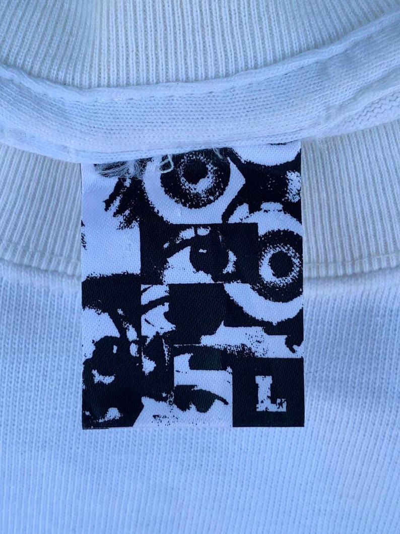 May include: White t-shirt with a black and white graphic print of eyes and the letter "L" on a tag.