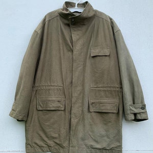 Könnte beinhalten: Eine langärmelige, olivgrüne Jacke mit Stehkragen, Reißverschluss und mehreren Taschen.