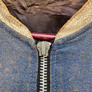Op de afbeelding: Close-up van een blauw leren jack met een zilveren rits. Het jack heeft een bruine leren kraag en is verweerd.