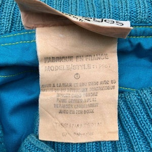 May include: A close-up of a blue and yellow fabric label with the text "FABRIQUE EN FRANCE" and "MODELE/STYLE: 13067" in black. The label also includes care instructions in French.