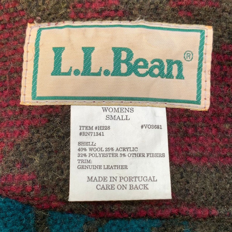 May include: A brown, green, and red plaid L.L.Bean jacket tag with the text "Womens Small" and the details "Item #H228 #RN71341 #VO3681" and the fabric composition "Shell: 40% Wool 25% Acrylic 32% Polyester 3% Other Fibers Trim: Genuine Leather" and the text "Made in Portugal Care on Back".