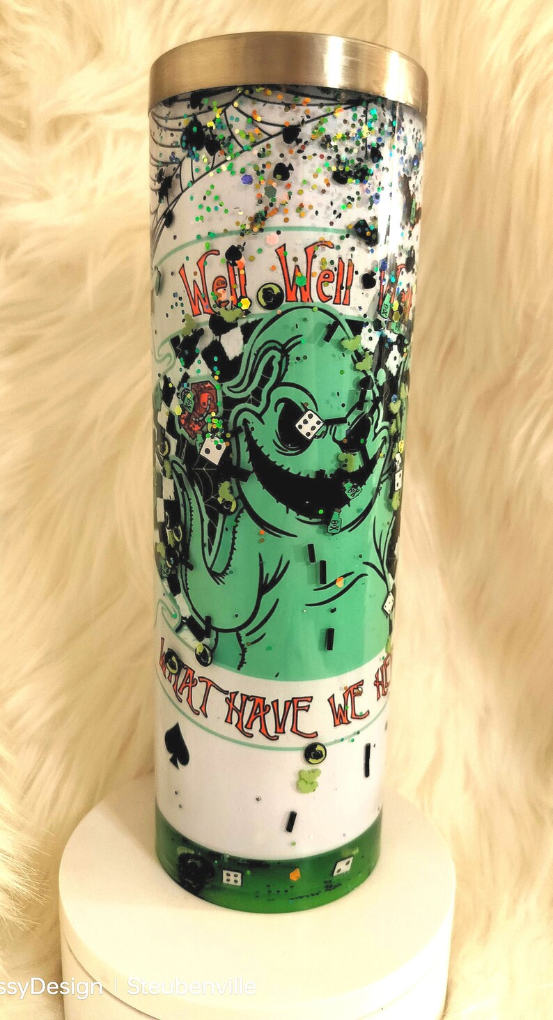 Może przedstawiać: Zielony i biały kubek z błyszczącym wykończeniem. Kubek przedstawia postać z kresk&oacute;wki z przebiegłym uśmiechem i tekstem "Well Well Well What Have We Here".