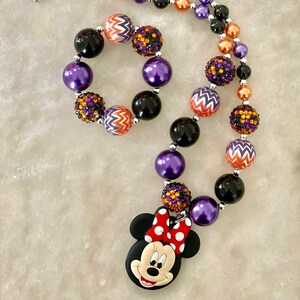 May include: A purple, orange, and black beaded necklace with a Minnie Mouse charm. The necklace is made with large, chunky beads and has a silver clasp.