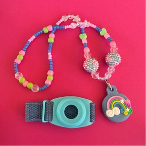 May include: A colorful beaded necklace with a rainbow charm and a blue and gray medical alert bracelet. The necklace has pink, blue, green, and white beads. The charm is a blue and gray silicone bracelet with a rainbow design.