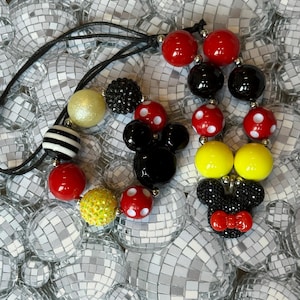 May include: A black cord necklace featuring colorful beads in red, black, yellow, and white. Some beads have polka dots or stripes. The necklace includes a Mickey Mouse and Minnie Mouse design.