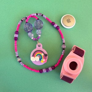 May include: A purple and pink beaded necklace with a rainbow charm and a pink and purple ID bracelet with a white circle in the center.