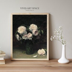 May include: A vintage painting of a bouquet of white roses in a green vase. The roses are arranged in a vase on a dark green table. The painting is framed in a light wood frame.