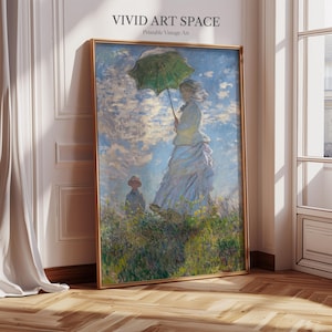 May include: A framed print of a vintage painting featuring a woman holding a green umbrella in a field. The artwork has a gold frame and the text "VIVID ART SPACE Printable Vintage Art" at the top. The painting depicts a sunny day with a blue sky and clouds.