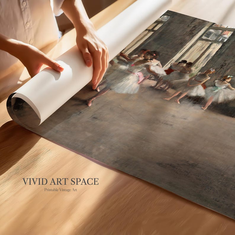 May include: A rolled-up print of a vintage painting featuring ballerinas in white tutus and pink ribbons. The print is being unrolled on a wooden surface. The text "VIVID ART SPACE Printable Vintage Art" is visible.