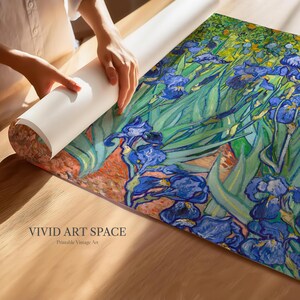 May include: A rolled-up print of a painting featuring blue irises and green foliage. The artwork is being unrolled on a wooden surface. The text "VIVID ART SPACE Printable Vintage Art" is visible at the bottom.