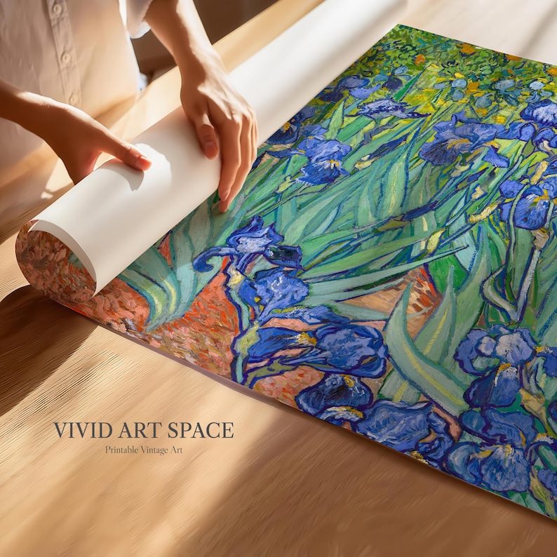 May include: A rolled-up print of a painting featuring blue irises and green foliage. The artwork is being unrolled on a wooden surface. The text "VIVID ART SPACE Printable Vintage Art" is visible at the bottom.