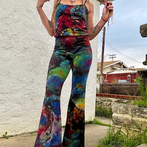 May include: A tie-dye two-piece set featuring a tank top and flared pants. The top and pants are a vibrant mix of colors, including red, blue, green, and yellow. The outfit is made of a soft, flowing fabric, perfect for a bohemian or festival look.