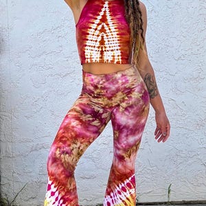 Könnte beinhalten: Ein zweiteiliges Tie-Dye-Set in Rot-, Rosa- und Gelbtönen. Das Set besteht aus einem Neckholder-Crop-Top und einer Schlaghose. Die Hose hat unten ein weißes und gelbes Tie-Dye-Muster.