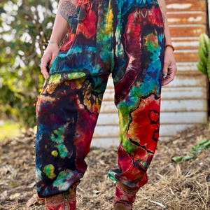 May include: Tie-dye sweatpants in a vibrant mix of colors including red, blue, green, and yellow. The pants have a drawstring waist and are cuffed at the ankles. The overall style is casual and bohemian.