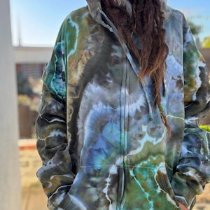 Może przedstawiać: Blu, zielona i brązowa bluza z kapturem zapinana na zamek, w stylu tie-dye. Bluza posiada kaptur ze sznurkiem i dwie przednie kieszenie. Wzór tie-dye tworzy unikalny, marmurkowy efekt. Zamek błyskawiczny biegnie przez środek.