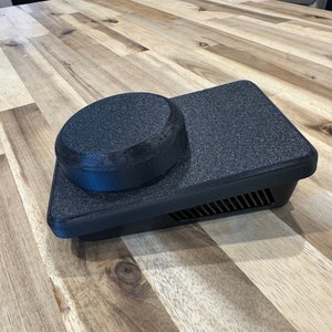 Peut inclure: Un objet rectangulaire noir texturé avec un bouton rond noir sur le dessus. L'objet est fait d'un matériau qui semble être du plastique ou du caoutchouc.