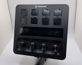 May include: A black Stream Deck with eight buttons, a small LCD screen, and four knobs. The device is mounted on a black stand.