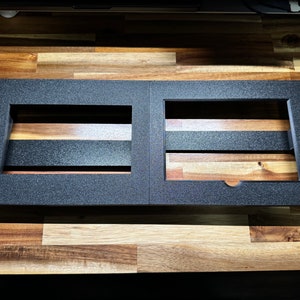 May include: Black metal pedalboard with two rectangular cutouts for pedals. The pedalboard is on a wooden surface.