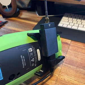 Op de afbeelding: Een groen en zwart medisch apparaat met een zwarte antenne. Het apparaat is gelabeld met "ETHERSCOPE NXG MODEL: EXG-200".