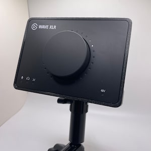 May include: Black Wave XLR audio interface with a large knob, headphone jack, and microphone input. The interface is mounted on a black adjustable stand. The text "WAVE XLR" and "48V" are visible on the interface.
