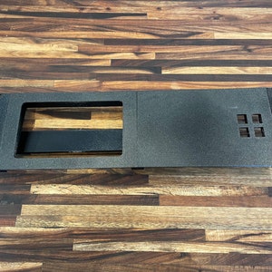 May include: A black metal rack with a rectangular cutout and a grid of four square holes. The rack is designed for mounting equipment.