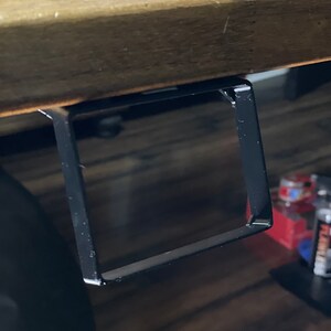 May include: Black metal shelf bracket attached to the underside of a wooden table.