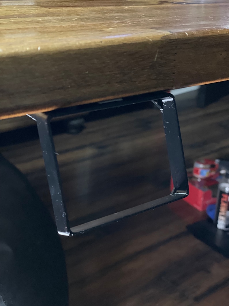 May include: Black metal shelf bracket attached to the underside of a wooden table.