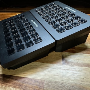 May include: Two black Stream Deck devices with a grid of buttons. Each button has a clear plastic cover.