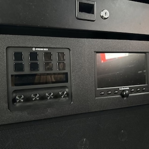 May include: A black Stream Deck with a small LCD screen and four knobs. The Stream Deck has a grid of nine buttons. The screen displays the text "tc electronic".