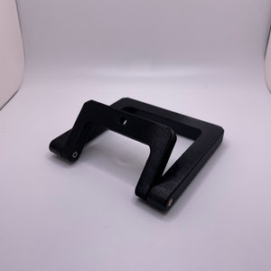 Może przedstawiać: Czarny, plastikowy stojak na telefon z możliwością złożenia. Stojak wykonany jest z fakturowanego materiału i ma prosty, nowoczesny design.