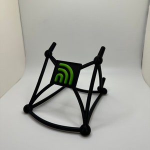 May include: Black phone stand with a green logo of a stylized signal bar. The stand is made of a flexible material and has a triangular shape.