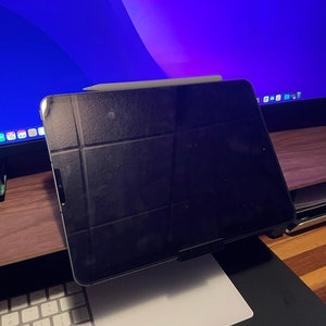 May include: A black iPad with a white Apple Pencil resting on top of it. The iPad is on a white stand and a white keyboard is in the foreground.