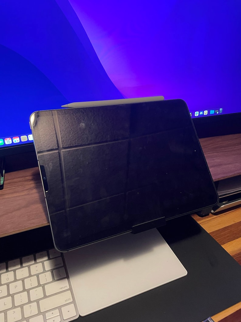 May include: A black iPad with a white Apple Pencil resting on top of it. The iPad is on a white stand and a white keyboard is in the foreground.