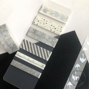 May include: A set of six washi tapes with different patterns, including marble, stripes, polka dots, and a silver glitter tape. The tapes are displayed on a clear plastic sheet with the text "love love" written on one of the tapes.