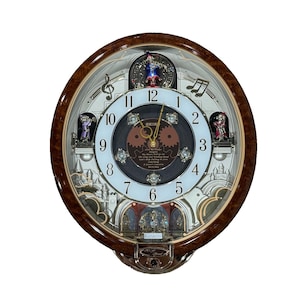 May include: An oval Seiko wall clock with a brown wood-grain frame. The white dial features black numerals, gold hands, and a central dark brown gear design with text listing song titles. Small figurines and musical notes decorate the clock face.