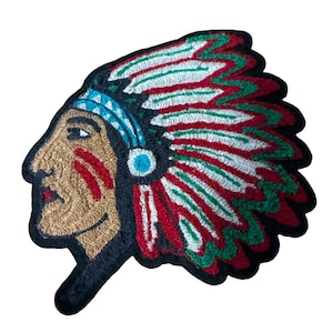 May include: An embroidered patch featuring a profile view of a person wearing a traditional feathered headdress. The design uses tan, red, white, green, and turquoise thread with a black border, depicting facial markings and a detailed headpiece.