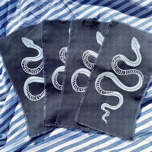 May include: Four dark blue fabric patches with a white snake design printed on each. The snake is curled in a 'S' shape with its head at the top of the patch.