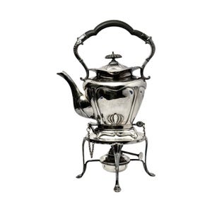 May include: Silver teapot with a black handle and a stand with a burner. The teapot has a rounded body with ornate details and a spout on the side.