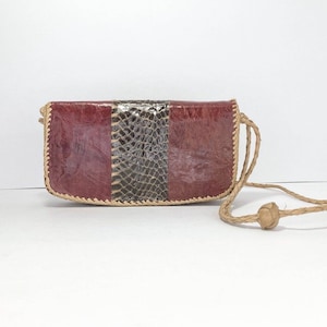 May include: A small, burgundy leather purse with a snakeskin panel and a braided rope strap.