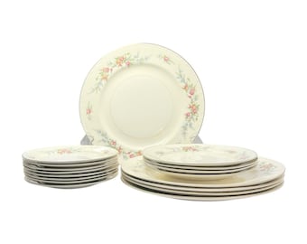 May include: A set of vintage floral dinnerware, featuring a cream-colored background with a delicate floral pattern in shades of pink and blue. The set includes dinner plates, salad plates, and bowls.