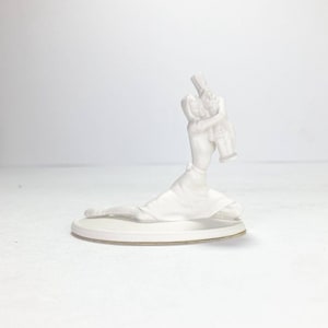May include: White ceramic figurine of a woman kneeling and holding a smaller figurine of a man in her arms.