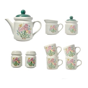 May include: A set of white ceramic kitchenware with a floral design. The set includes a teapot, creamer, sugar bowl, salt and pepper shakers, and four mugs.